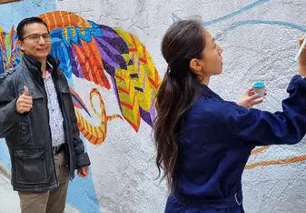 A man gives a thumbs up as a woman paints a wall.