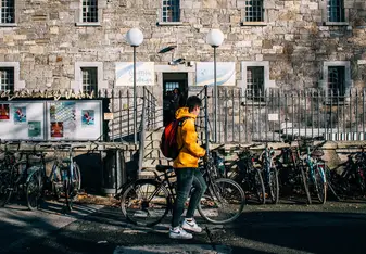 A man with a bike stands in front of a university building.