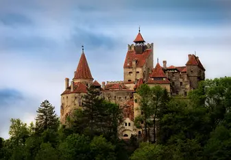 A medieval castle rests atop a tree-lined hill within the mountains of Romania