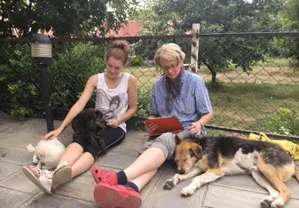 Two volunteers sit with two dogs 