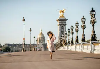 Woman wearing a hat walks across a bridge in Paris.