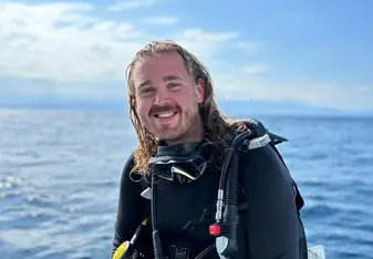 A happy male diver sitting on the edge of the dive boat in full gear smiling at the camera
