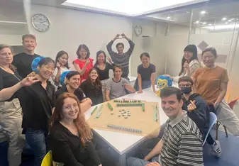Students sitting and standing around a table watching peers play Mahjong