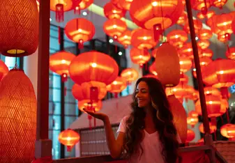 A woman stands in a room full of red lanterns.
