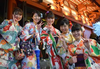 Smiling women in kimonos give the peace sign.