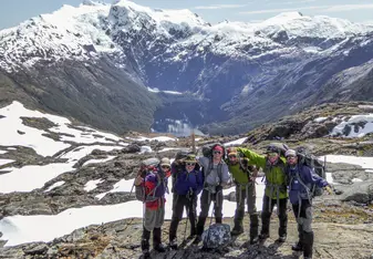 NOLS students stand for a photo in front of a snow capped peak