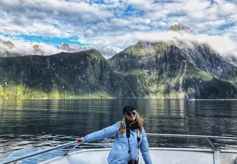 A woman stands on a boat with mountains in the background.
