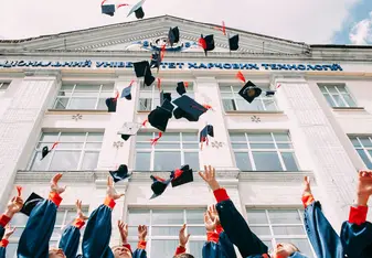 College graduates toss their caps in the air in front of a building.