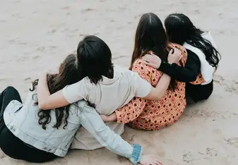 Friends with their arms around each other sit on the beach.