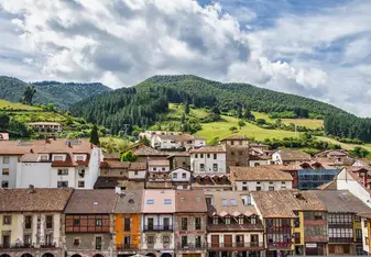 A scenic Spanish village with colorful, traditional houses nestled at the base of lush green hills covered in pine trees. The vibrant architecture and serene countryside reflect the charm and beauty that RVF International participants experience while exploring Spain’s hidden treasures.