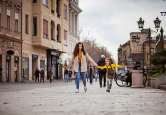 A woman holds hands with a little girl in the street.