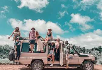 A group of people sit or stand around a safari jeep.