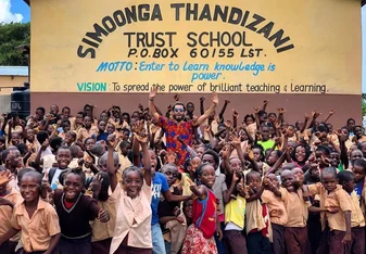 Volunteer cheering with children outside Simoonga. 