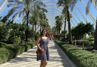 A young woman in a summer dress poses in Valencia’s stunning architectural garden surrounded by towering palm trees and bright blue skies. The symmetrical arches create a dreamy pathway, capturing the beauty and charm of exploring Spain with RVF International.