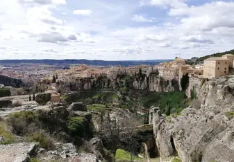 Historic hanging houses perched on the cliffs of Cuenca, Spain, overlooking a dramatic gorge with a panoramic view of the medieval city and surrounding countryside.