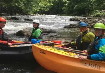 Crew in kayaks on a white water river, on the river bank look over for a picture.