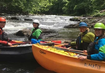 Crew in kayaks on a white water river, on the river bank look over for a picture.