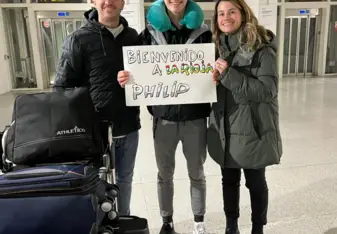 International student arriving in Spain, warmly welcomed by his host family at the airport with a sign saying "Welcome to La Rioja".