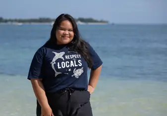 Tania smiling at the camera in front of a beautiful turquoise blue ocean back drop