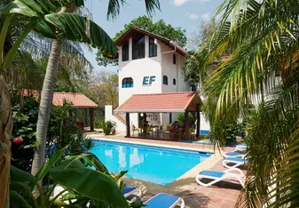 EF Tamarindo campus in Costa Rica with a pool surrounded by palm trees, lounge chairs, and tropical buildings where students live and study abroad.