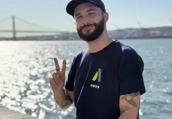 Bastien smiles and holds up a peace sign on a sunny day in front of the ocean