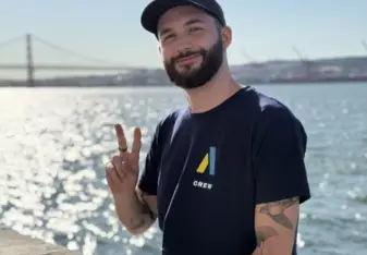 Bastien smiles and holds up a peace sign on a sunny day in front of the ocean