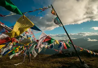 Prayer flags flying in the wind in the mountains of Bhutan with large clouds above in a light blue sky