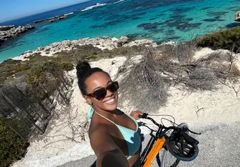 A girl on a bike taking a selfie with a blue sea behind her.