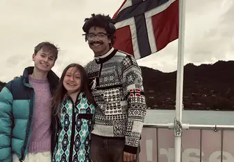 three college students stand smiling with the Norwegian flag waving in the wind