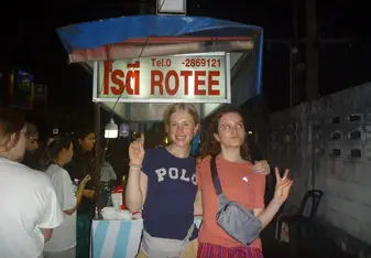Two girls standing in front of a rotee street food cart 