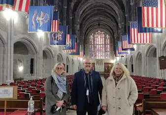 image of three smiling people in a hall with American flags hanging from the ceiling