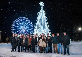 smiling students and teachers in front of colorful christmas tree with lights and ferris wheel