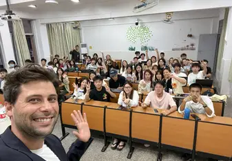 Smiling male TEFL teacher takes a selfie with a classroom full on students.