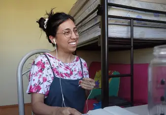 Smiling female TEFL teacher in bedroom teaching English online.