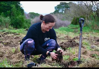 Woman kneeling in field while tending to plant