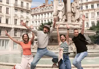 four people jumping in front of a historic fountain