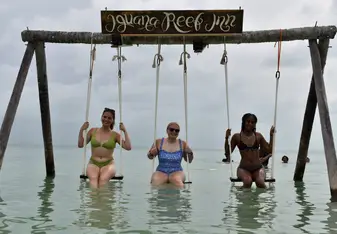 Three teen travelers sitting on a swing in the ocean in Belize