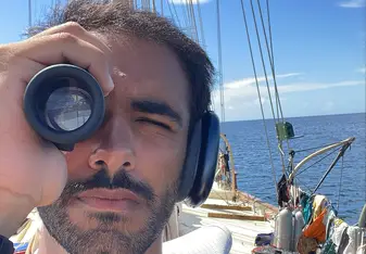 Mohamed AlDakheel looks through a navigation instrument on the deck of a sailboat at sea