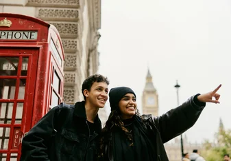 Two tourists smiling in front of telephone booth and clock tower in London