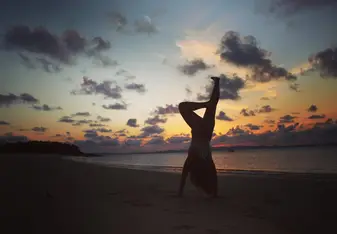 silhouette of person doing handstand on beach at sunset