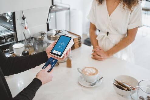 A merchant entering a credit card into a card reader at a cafe counter