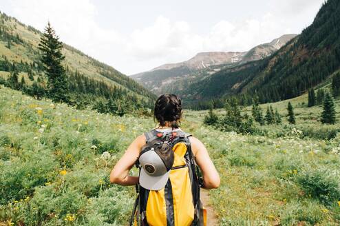 A girl with a yellow backpack hikes through lush, green landscapes in the mountainns