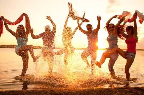 Happy people splashing in the ocean at sunset.