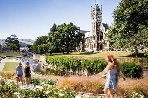 A couple young students walk on campus by a gothic building
