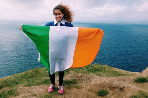A student poses on a cliff with the Irish flag