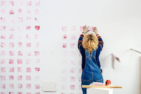 Student working on a piece of art, pink squares on a wall.