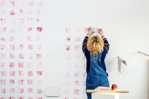 Student working on a piece of art, pink squares on a wall.