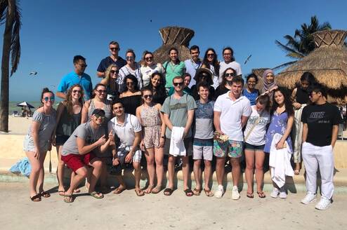 A group photo of participants in front of a hut on the sunny beach