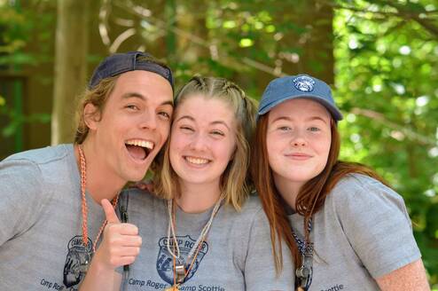 Image of 3 young adults smiling together in the woods