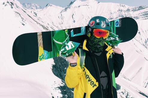 Snowboarder holding board in green and yellow jacket with helmet